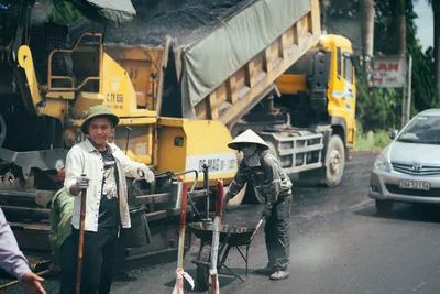 Men working on paving a road with construction machinery and vehicles.
