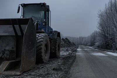 A large bulldozer positioned by a frosty road in a wintery forest.